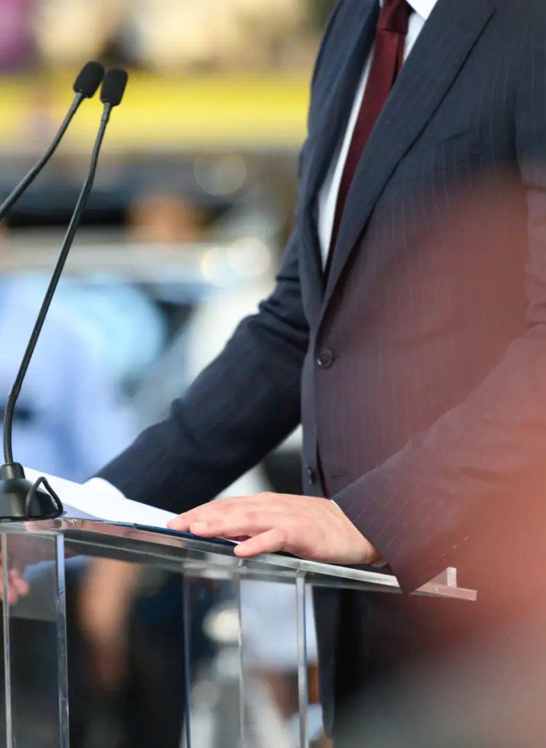 Suit-clad speaker at podium with microphones